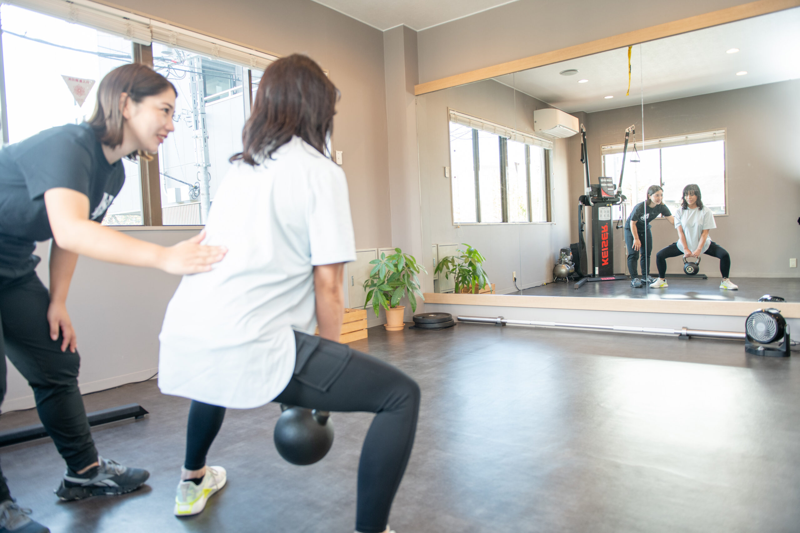 トレーナーが姿勢をチェックしながらアドバイスするジムの様子(女性が立位で姿勢測定を受けているシーン)